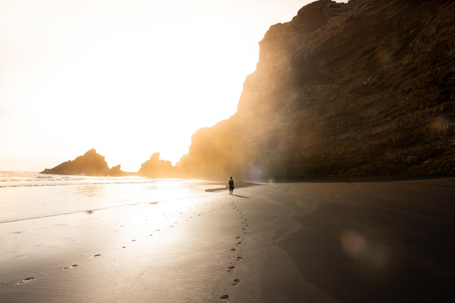 A lone person walks on the beach as the sun rises on the horizon